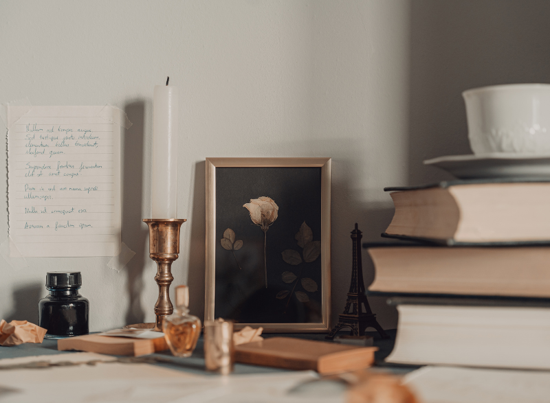A rustic collection of old books, candles, calligraphy pens and a cup of tea perched on a desk.