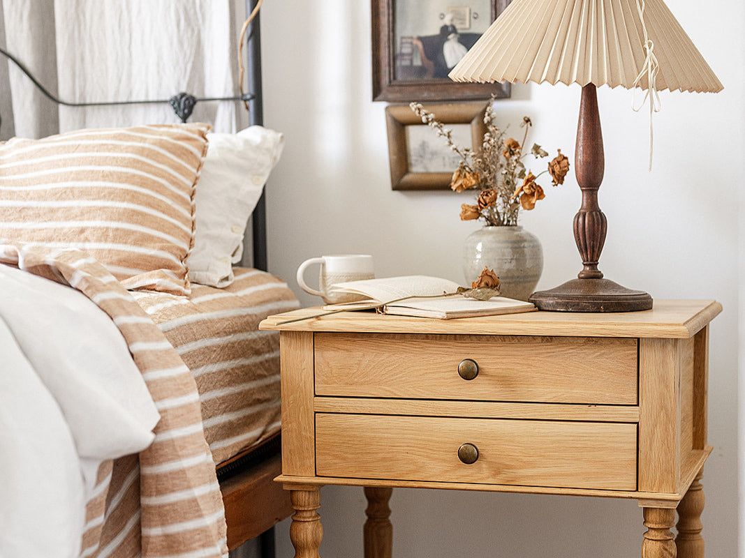 A French Provincial bedroom with a bedside table with a lamp and vase next to a bed dressed with linen sheets